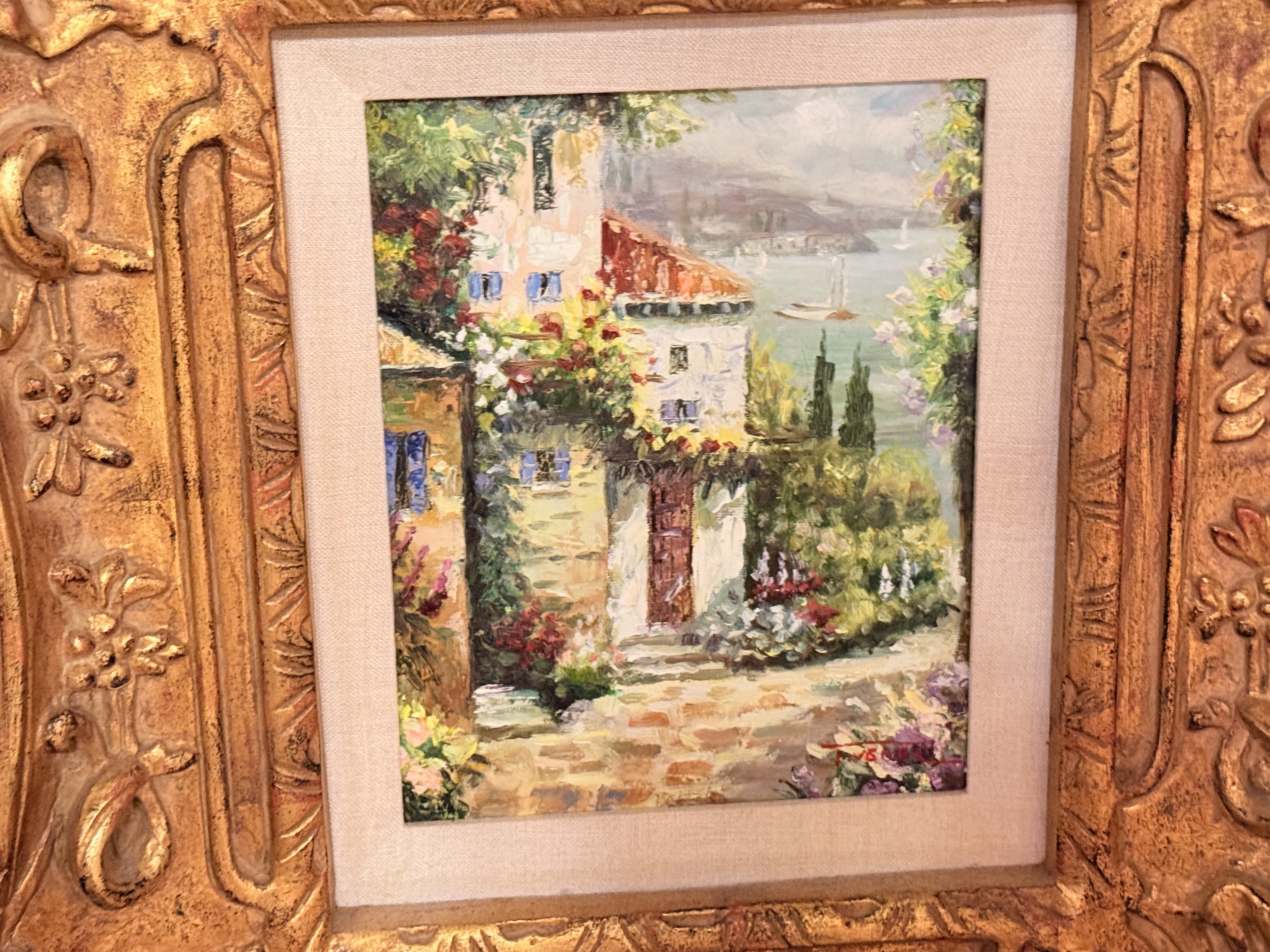 Painting of a flowered village lane in a carved gilt frame.